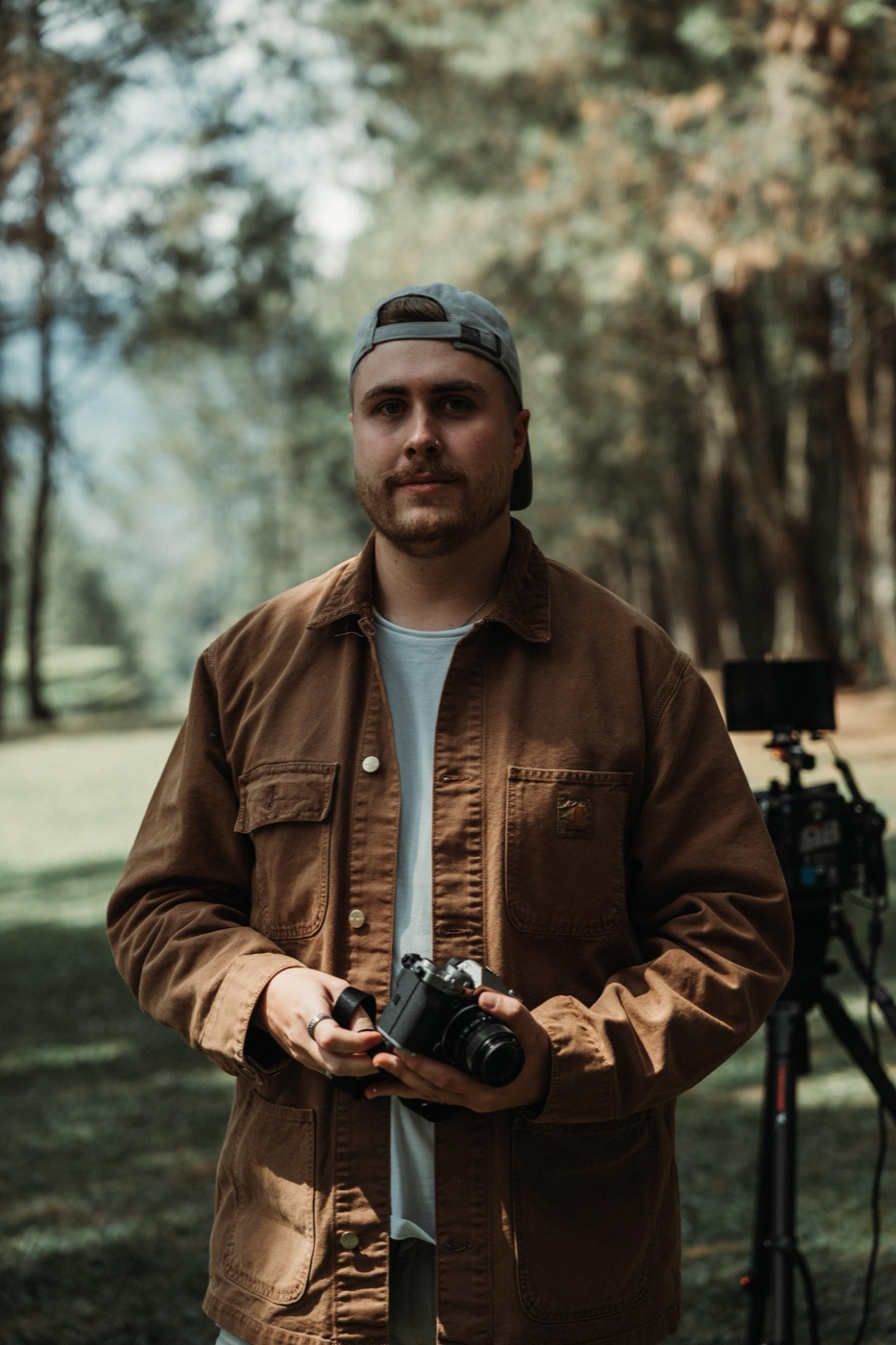 Matt Benn on set in a pine forest, film camera in hand, cinema rig behind him