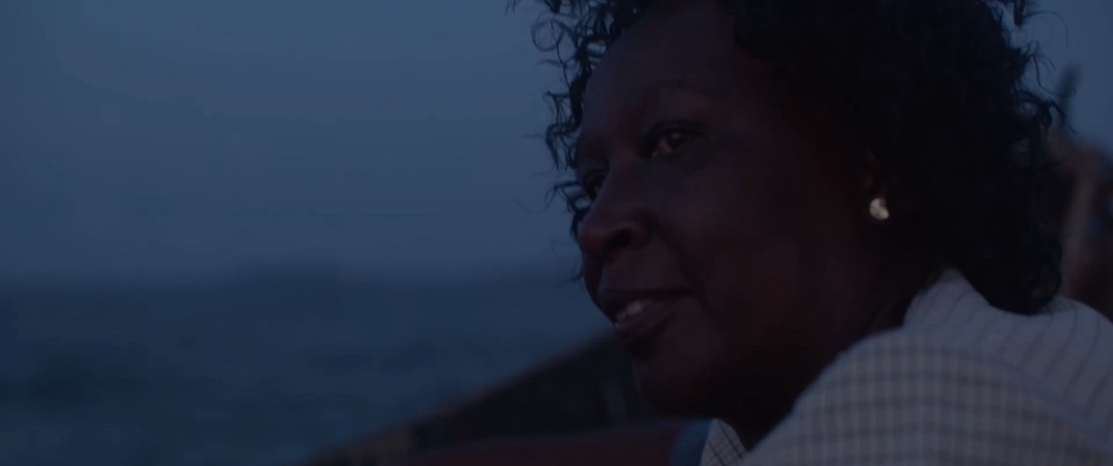 A frame from the reel: a woman on a wooden boat at blue hour, gazing across the water