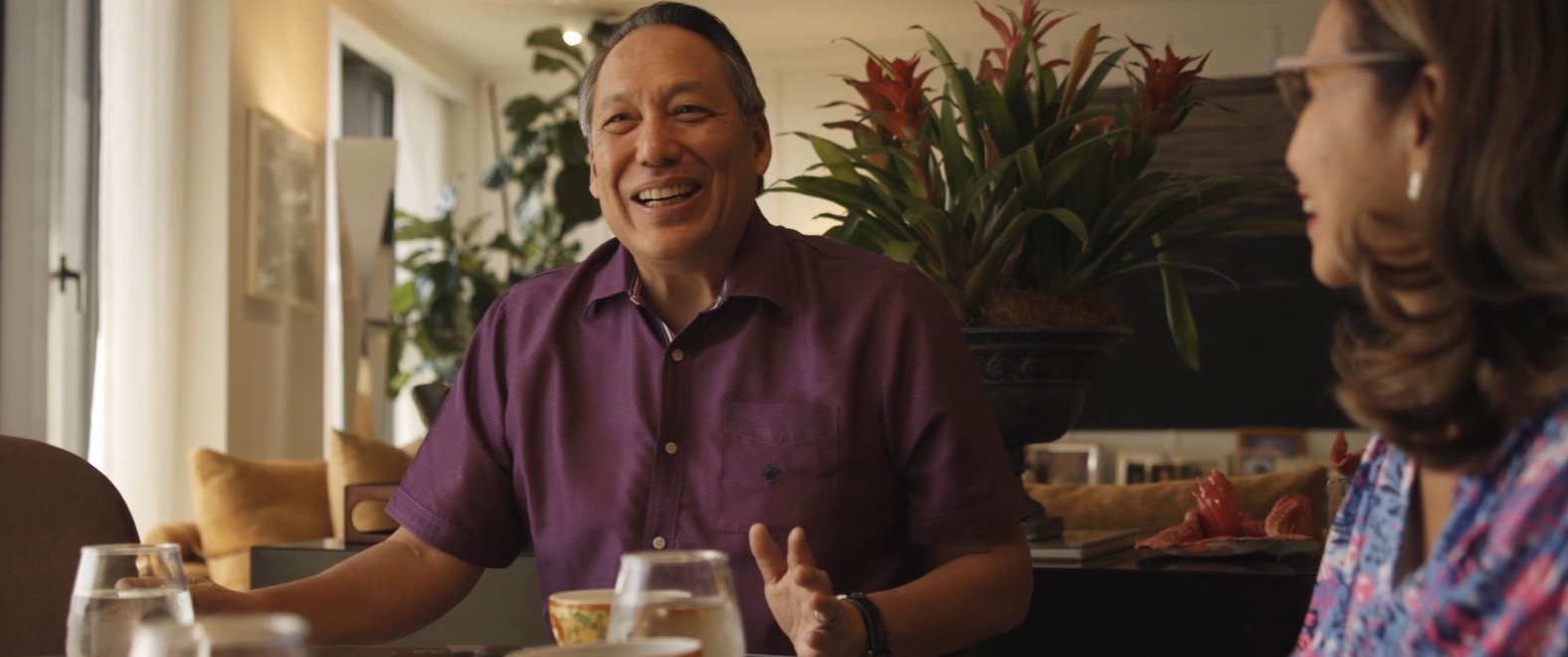 A frame from the reel: a man laughing mid-conversation at a table during a home interview