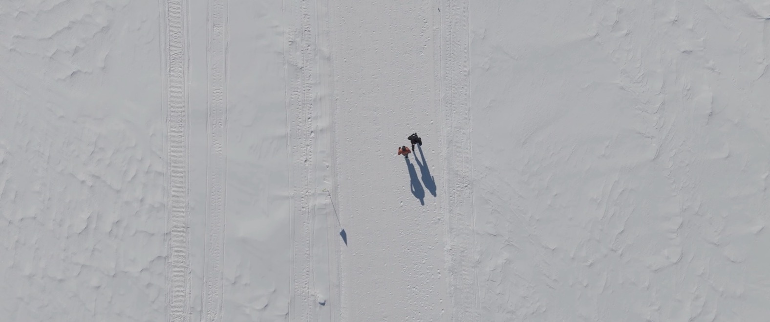 A frame from the reel: two figures crossing a vast snowfield seen from above