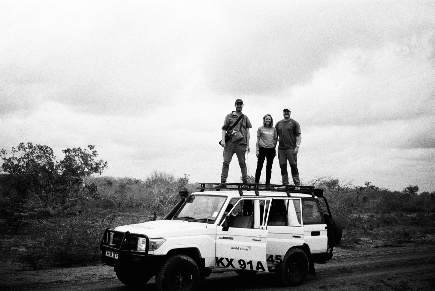 The crew standing on a Land Cruiser in rural Kenya, Matt Benn in the middle, black and white